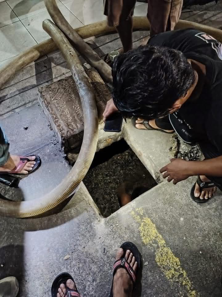 Crew inspecting an opened manhole at night with hoses ready